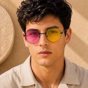 May include: Round sunglasses featuring a thin black metal frame with mismatched lenses. The left lens is a vibrant pink, while the right lens is a bright yellow. The glasses have a simple bridge and slim temples, providing a distinct look.