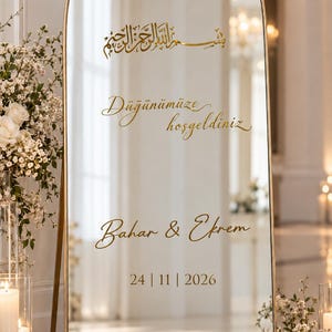 Könnte beinhalten: Ein gewölbter Standspiegel mit einem dünnen goldenen Rahmen und goldener Schrift mit dem Text Bismillah, Düğünümüze hoşgeldiniz, Bahar & Ekrem sowie dem Datum 24 | 11 | 2026. Die Spiegelfläche zeigt den umliegenden Raum.