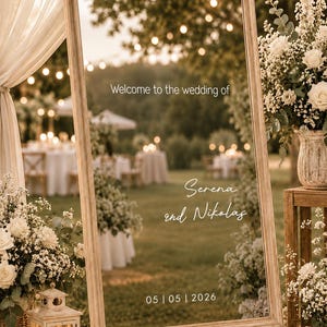Könnte beinhalten: Ein hoher rechteckiger Spiegel mit hellem Holzrahmen, der auf einer Holzstaffelei steht. Auf dem Glas befindet sich ein weißer Schriftzug mit dem Text "Welcome to the wedding of", "Serena and Nikolas" und dem Datum "05 | 05 | 2026".