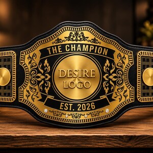 Könnte beinhalten: Ein Meistergürtel mit einem schwarzen Lederriemen und einer großen, goldfarbenen Metallplatte in der Mitte. Die Platte zeigt den Text THE CHAMPION, DESIRE LOGO und EST. 2026, umgeben von goldenen Filigranmustern und kleinen runden Akzenten.
