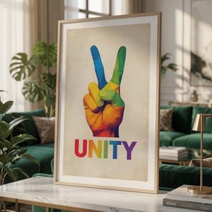 Könnte beinhalten: Ein gerahmter Kunstdruck, der eine Hand zeigt, die ein Friedenszeichen mit einem lebendigen Regenbogen-Farbverlauf bildet. Unter der Hand steht das Wort UNITY in fetten, mehrfarbigen Großbuchstaben auf einem hellbeigen Hintergrund.