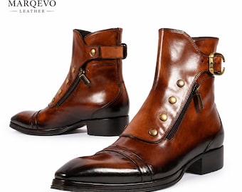 May include: A pair of burnished brown leather ankle boots featuring a pointed toe, a side zipper closure, and a decorative strap with a brass buckle. The boots are accented with a row of brass studs along the side and the Marqevo Leather logo.