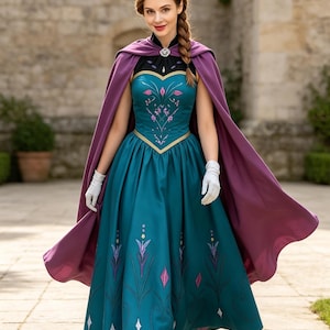 May include: A teal floor-length dress with a black bodice, a heart-shaped neckline, and pink and purple floral embroidery. The dress features a long purple cape fastened with a silver brooch and is paired with white gloves and black boots.