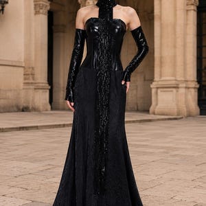 Pode incluir: Um vestido preto longo até ao chão com um corpete tipo espartilho sem alças em pele sintética brilhante e uma saia longa texturizada. O conjunto inclui uma gola alta com um painel longo de franjas de missangas e luvas compridas a condizer.