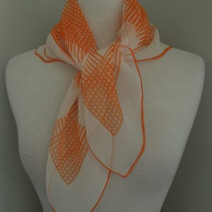 May include: A square scarf featuring a white base with a geometric pattern of orange dots and stripes. The scarf has a thin orange border along the edges and is tied in a simple knot, displaying a lightweight, semi-sheer fabric construction.