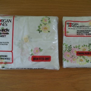 May include: Two sealed packages of Morgan Jones No-Iron luxury muslin sheets and pillowcases. The queen fitted sheet package is on the left, and the standard pillowcases are on the right. Both packages feature a floral pattern with pink and yellow flowers.
