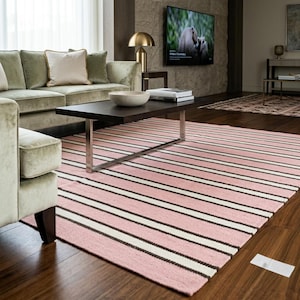 May include: A rectangular area rug featuring a repeating pattern of wide pink stripes alternating with thinner white and dark brown stripes, covering a dark wood floor in a living room setting with a light green sofa and a dark brown coffee table.