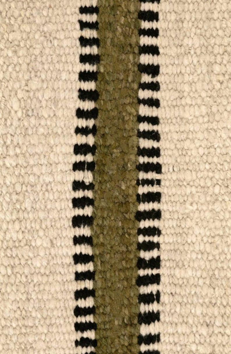 Hand woven wool area rug in cream, olive green, and black with a modern striped pattern, featuring a textured flatweave design and neutral colors, shown in close-up and contemporary living room settings. Handmade minimalist rug for living room, bedroom, office, or entryway decor.