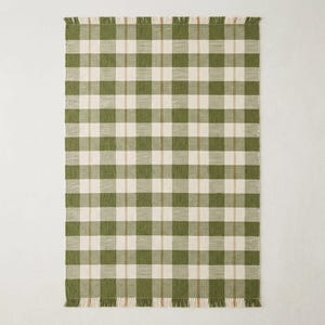 Peut inclure: Un tapis tissé rectangulaire présentant un motif à carreaux vert et blanc cassé avec de fines rayures verticales beiges traversant le centre des carrés blancs. Le tapis est fini avec des franges courtes et droites sur les bords.