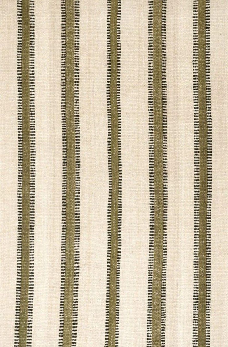 Hand woven wool area rug in cream, olive green, and black with a modern striped pattern, featuring a textured flatweave design and neutral colors, shown in close-up and contemporary living room settings. Handmade minimalist rug for living room, bedroom, office, or entryway decor.