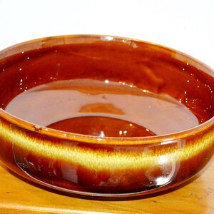 Puede incluir: Un cuenco redondo de cerámica con un esmalte brillante de color marrón oscuro en el interior y el exterior, acentuado por una banda horizontal ancha de esmalte de goteo amarillo dorado más claro que rodea la pared exterior.