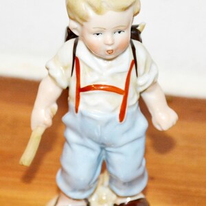 Vintage porslinsfigur av en skolpojke från 1950-talet, med motiv av en get och en damm. Retro, Ostalgie, shabby chic, tillverkad i Östtyskland (DDR), modern stil i mitten av århundradet.