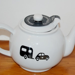 Könnte beinhalten: Eine weiße Teekanne aus Keramik mit einer schwarzen Grafik eines Autos, das einen Wohnwagen zieht. Auf dem Deckel befindet sich ein schwarzes, rundes Etikett mit dem weißen Aufdruck Price & Kensington und 6 Cup. Die Kanne hat einen Henkel und Ausguss.