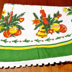 Könnte beinhalten: Eine weiße Tischdecke mit einem festlichen Druck aus roten Kerzen, gelben Glocken, grünen Tannenzweigen sowie roten und gelben Ornamenten. Der Stoff hat einen breiten grünen Rand mit einem gelben Streifen und einem weißen Spitzenbesatz.