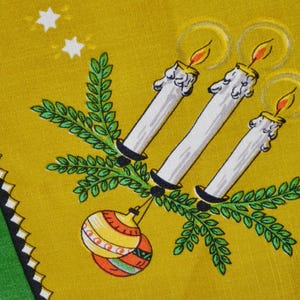 Peut inclure: Un tissu jaune moutarde avec un motif imprimé de trois bougies blanches aux flammes orange, des branches de pin vertes et deux boules décoratives. La bordure présente une bande verte avec un motif en zigzag noir et blanc et des étoiles blanches.