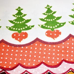 Könnte beinhalten: Ein weißer Stoffläufer mit einem wiederkehrenden Muster aus grünen Weihnachtsbäumen mit weißen Punkten, die jeweils auf einem roten Herz stehen. Der untere Rand hat eine gewellte Borte aus rot-weiß gepunktetem Stoff mit dunkelrotem Saum.