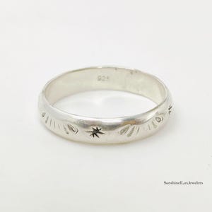 Puede incluir: Un anillo de banda de plata con motivos grabados de estrellas y rayos de sol en la superficie exterior. El interior de la banda está claramente marcado con el número 925, lo que indica plata de ley. El texto SunshineLuxJewelers es visible.