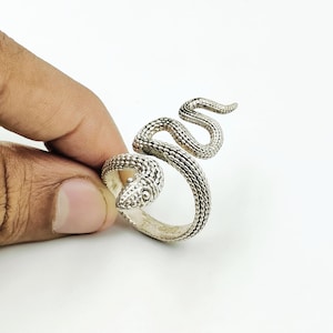May include: A silver-toned ring shaped like a coiled snake with a textured, scale-like surface. The snake's head is positioned at the front of the band, while its body wraps around to form the circular ring shape with a detailed, bumpy finish.