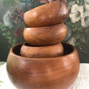 May include: A stack of four wooden bowls in varying sizes. The bowls are a warm brown color with visible wood grain. The largest bowl is at the bottom, with three smaller bowls nested inside. The bowls appear to be handmade and have a smooth, polished finish.