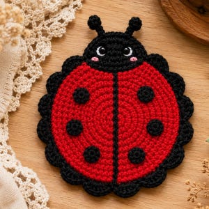 May include: A round, crocheted ladybug coaster featuring a vibrant red body with six black circular spots and a black head with two antennae. The ladybug has white eyes with black pupils and small pink cheeks, finished with a scalloped black border.