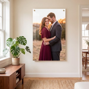 Peut inclure: Une grande impression murale rectangulaire en acrylique représentant un portrait de deux personnes s'enlaçant en extérieur au coucher du soleil. La personne à gauche porte une robe bordeaux, celle à droite un costume gris foncé. Fixations dorées.