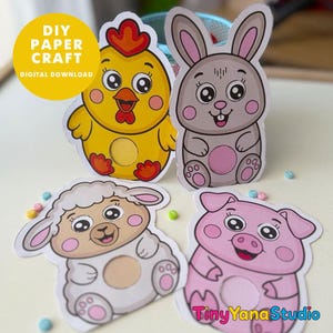 May include: Four paper cutouts featuring cartoon animals: a yellow chick, a gray rabbit, a white sheep, and a pink pig. Each animal has a circular cutout in the center and large eyes. Text reads DIY PAPER CRAFT DIGITAL DOWNLOAD and TinyYanaStudio.