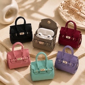 Può includere: Una collezione di sei custodie in miniatura a forma di borsa per auricolari wireless. Le custodie sono disponibili in nero, grigio, bordeaux, rosa, turchese e viola. Ognuna presenta due manici, una chiusura metallica dorata e una patta.