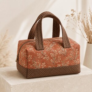May include: A rectangular fabric bag with two handles, featuring a rust-orange base color with a delicate white floral pattern. The bottom section and handles are made of a contrasting dark brown fabric with a fine white polka dot pattern.