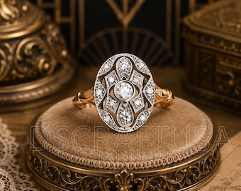 May include: An oval-shaped ring featuring a central round diamond surrounded by smaller diamonds set in a white metal filigree frame, mounted on a polished yellow gold band. The intricate metalwork creates a geometric pattern around the stones.