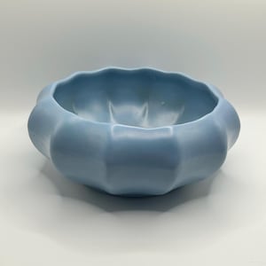 Peut inclure: Un bol en céramique bleu clair avec un bord festonné en forme de pétales et une finition mate lisse. Le bol présente un corps large et arrondi avec des indentations verticales profondes sur l'extérieur, créant une forme de fleur distincte.