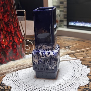Peut inclure: Un vase en céramique haut et carré avec une finition bleu foncé brillante. La partie inférieure du vase présente un motif d'émail texturé coulant en blanc et bleu, créant un contraste marqué avec le col supérieur en bleu foncé uni.