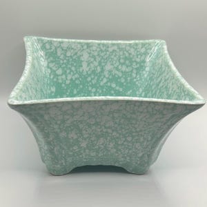May include: A square-shaped bowl featuring a light mint green base colour with a white speckled, splatter-style pattern across the entire exterior and interior surface. The bowl has flared sides and a wide opening with a curved, four-footed base.
