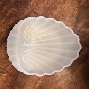 Peut inclure: Un plat blanc translucide en forme de coquillage avec un bord festonné et des crêtes rayonnantes. Le plat présente une finition lisse et brillante ainsi qu'une forme concave incurvée qui imite l'apparence d'un coquillage naturel.