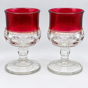 Peut inclure: Une paire de verres à pied dotés d'un bol supérieur en verre rouge profond et d'une base en verre transparent. La section en verre clair présente un motif texturé en relief au milieu, tandis que le pied et la base circulaire sont lisses.