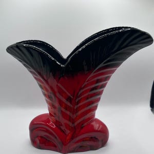 May include: A ceramic vase featuring a flared, fan-like silhouette with a glossy finish. The base is a vibrant red that transitions into a deep black at the wide, scalloped rim. The surface displays a textured, ribbed pattern throughout.