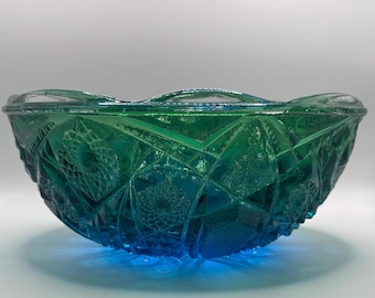 Puede incluir: Un cuenco de cristal de color verde esmeralda intenso con un complejo patrón prensado de líneas geométricas entrelazadas, formas de diamante y motivos de estrella. El cuenco tiene un borde festoneado y una estructura gruesa y translúcida.
