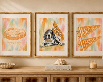 May include: Three framed art prints featuring orange and white watercolor backgrounds. The left print shows Neyland Stadium, the center print depicts a dog wearing a VOLS bandana with a matching flag, and the right print displays two pennants labeled Knoxville and Tennessee.