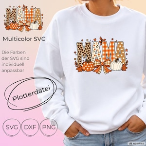 Op de afbeelding: Een wit sweatshirt met lange mouwen en een grafische print van het woord MAMA in blokletters. De letters hebben patronen zoals luipaardprint, oranje ruitjes en bruine stippen, versierd met oranje pompoenen en een geruite strik.