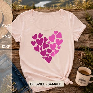 Può includere: Una t-shirt a maniche corte rosa chiaro con una grande grafica a forma di cuore composta da diversi cuori più piccoli in varie tonalità di rosa e magenta. La maglietta presenta uno scollo rotondo e un orlo annodato sul lato destro.