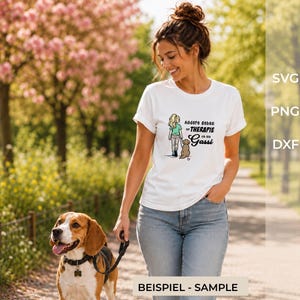 Può includere: Una t-shirt bianca a maniche corte con la grafica di una persona che porta a spasso un cane e il testo in tedesco "Andere gehen zur THERAPIE ich geh Gassi" stampato in nero. Il design include una piccola icona a cuore rosa vicino al cane.