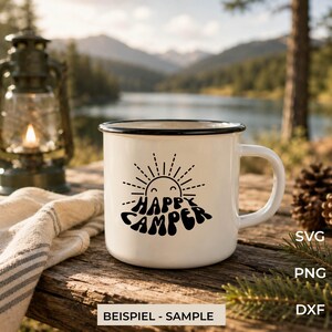 May include: A white enamel mug with a black rim and a black graphic print of a sun and the text HAPPY CAMPER. The mug features a handle on the right side and is positioned on a wooden surface. The text SVG, PNG, DXF, and BEISPIEL - SAMPLE is visible.
