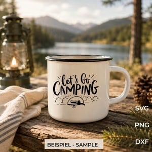 Könnte beinhalten: Ein weißer Emaillebecher mit schwarzem Rand und einem schwarzen Grafikdruck, der "let's go CAMPING" über einer Illustration eines kleinen Wohnwagens zeigt. Der Becher hat einen Henkel auf der rechten Seite und steht auf einer Holzoberfläche.