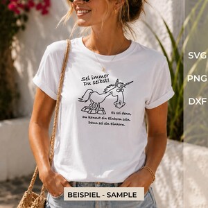 Puede incluir: Una camiseta blanca de manga corta con un dibujo lineal negro de un unicornio de dibujos animados. El texto sobre el unicornio dice "Sei immer Du selbst!" y el texto debajo dice "Es sei denn, Du kannst ein Einhorn sein. Dann sei ein Einhorn."
