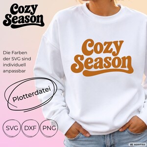Könnte beinhalten: Ein weißes Langarm-Sweatshirt mit dem Text Cozy Season in einer fetten, braunen Retro-Schriftart. Das Design ist mittig auf der Brust platziert. Das Bild enthält zusätzlichen Text und Symbole, die Dateiformate wie SVG, DXF und PNG angeben.
