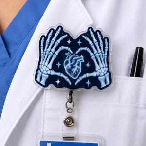 Może przedstawiać: Identyfikator z ciemnoniebieską akrylową nakładką przedstawiającą jasnoniebieskie szkieletowe dłonie tworzące kształt serca wokół centralnego anatomicznego serca. Wzór zawiera małe białe gwiazdki i jest przymocowany do zwijanej linki.