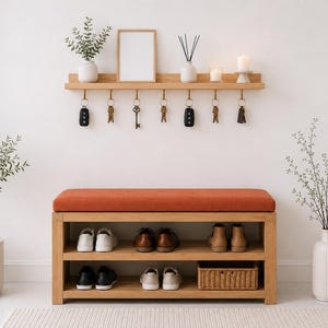 K&ouml;nnte beinhalten: Eine Schuhbank aus hellem Holz mit orangefarbenem Polstersitz und zwei offenen Regalen f&uuml;r verschiedene Schuhe und einen Weidenkorb. Dar&uuml;ber befindet sich ein passendes Wandregal mit sieben Metallhaken f&uuml;r Schl&uuml;ssel und Dekoration.