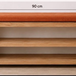 K&ouml;nnte beinhalten: Eine rechteckige Holzbank mit einem rostorange gepolsterten Sitz und zwei offenen Ablagef&auml;chern. Die Bank misst 90 cm in der L&auml;nge, 30 cm in der Tiefe und 45 cm in der H&ouml;he, wie durch die Ma&szlig;linien im Bild deutlich gekennzeichnet ist.