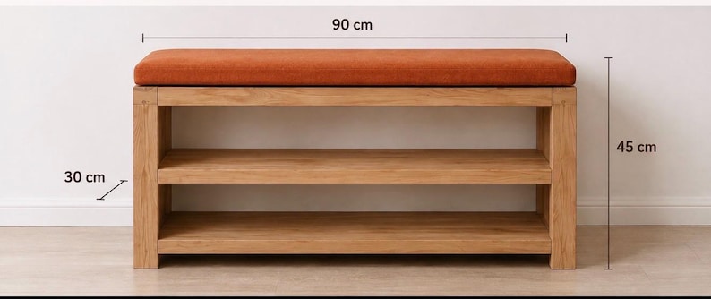 K&ouml;nnte beinhalten: Eine rechteckige Holzbank mit einem rostorange gepolsterten Sitz und zwei offenen Ablagef&auml;chern. Die Bank misst 90 cm in der L&auml;nge, 30 cm in der Tiefe und 45 cm in der H&ouml;he, wie durch die Ma&szlig;linien im Bild deutlich gekennzeichnet ist.
