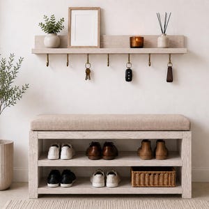 K&ouml;nnte beinhalten: Eine helle Holz-Eingangsbank mit beigem Polstersitz und zwei offenen Regalen f&uuml;r Schuhe und einen Weidenkorb. Dar&uuml;ber befindet sich ein passendes Wandregal mit sieben Messinghaken, an denen Schl&uuml;ssel und ein Schl&uuml;sselanh&auml;nger h&auml;ngen.