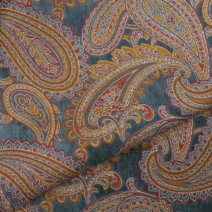 Può includere: Un tessuto caratterizzato da un fitto motivo paisley nei toni del blu spento, giallo senape e rosso scuro. I complessi motivi a goccia sono collegati da sottili linee bianche, creando un disegno continuo su tutta la superficie.